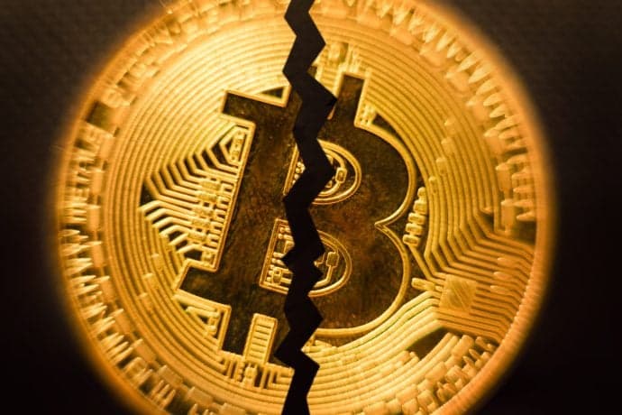 Eine goldene Bitcoin-Münze mit einem markanten, gezackten Riss in der Mitte, der die finanzielle Instabilität oder Störung von Bitcoin symbolisiert.